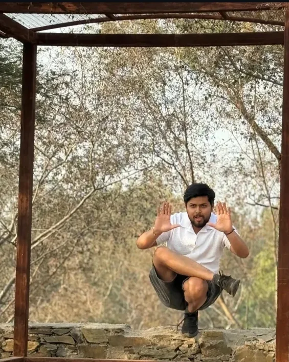 Yoginder crouched mid-air inside a wooden frame with his hands held up like a director framing a shot